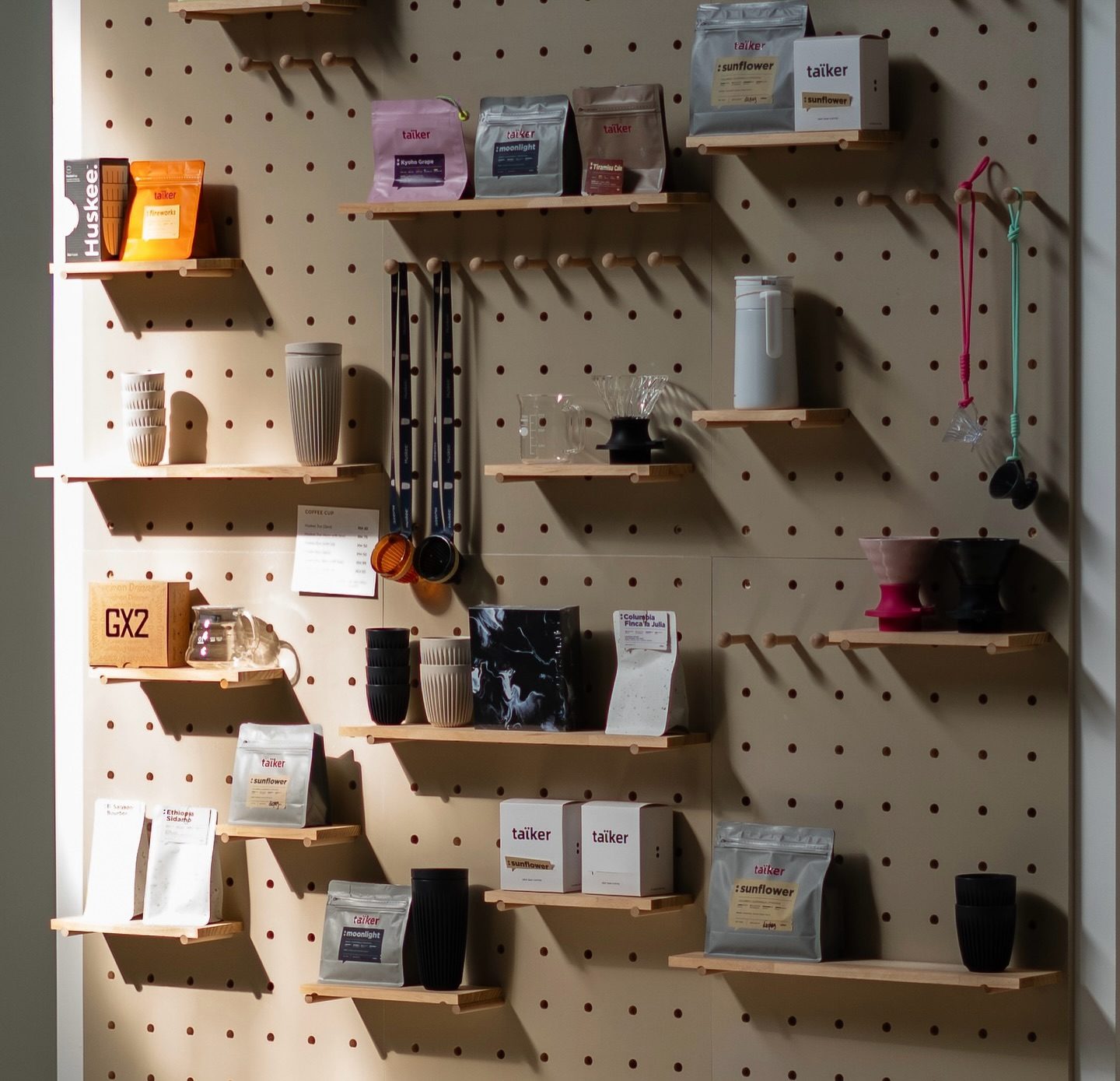The taïker counter — bags of beans, Huskee cups and brewing gear on a pegboard wall.