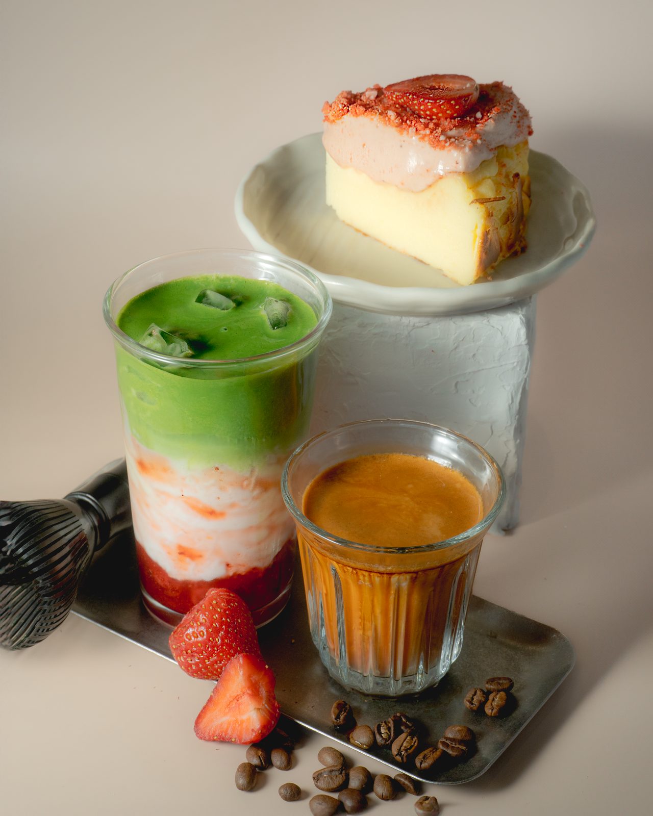 A taïker spread — an iced strawberry matcha, a glass of espresso and a slice of strawberry basque cheesecake.